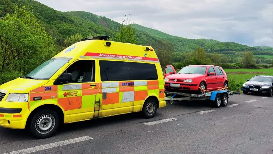 Příslušníci dálniční policie kontrolují vozidlo připomínající sanitku, které vezlo osobní auto na přívěsu – případ skončil ve správním řízení kvůli nelegálnímu výstražnému zařízení.